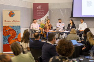 Panel discussion on stage with five speakers and audience listening, banners for Dhawura Ngilan and RIaa Australia in the background.
