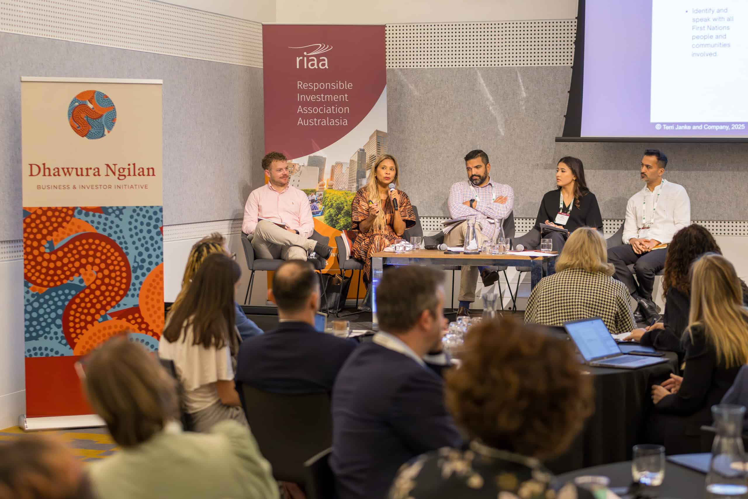 Panel discussion on stage with five speakers and audience listening, banners for Dhawura Ngilan and RIaa Australia in the background.
